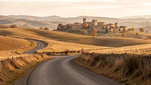 Route sinueuse traversant un plateau doré de Castille-et-León en automne, avec un village médiéval au loin dans la lumière douce de la fin d’après-midi.